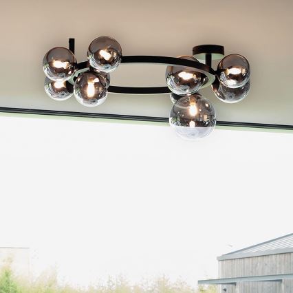 Stropné svietidlo s oválnym čiernym rámom drží osem tmavosivých sklenených gúľ. Svietidlo je pripevnené k stropu.