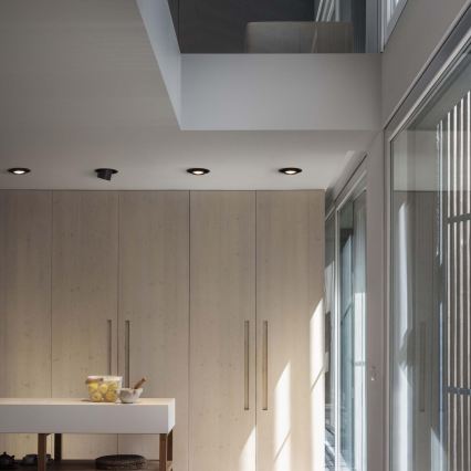 Tri vstavané bodové svetlá sú osadené v bielom strope. Dve sú valcovité, jedno ploché. Svetlá svietia smerom nadol. Pod stropom je biela stena.