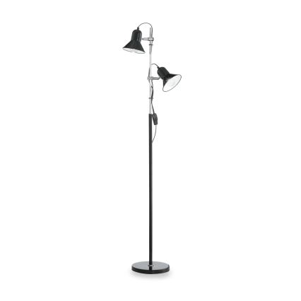 Stojacia lampa s dvoma čiernymi tienidlami na nastaviteľných ramenách svieti. Má vysokú čiernu nohu a okrúhlu základňu. Lampa je na bielom pozadí.