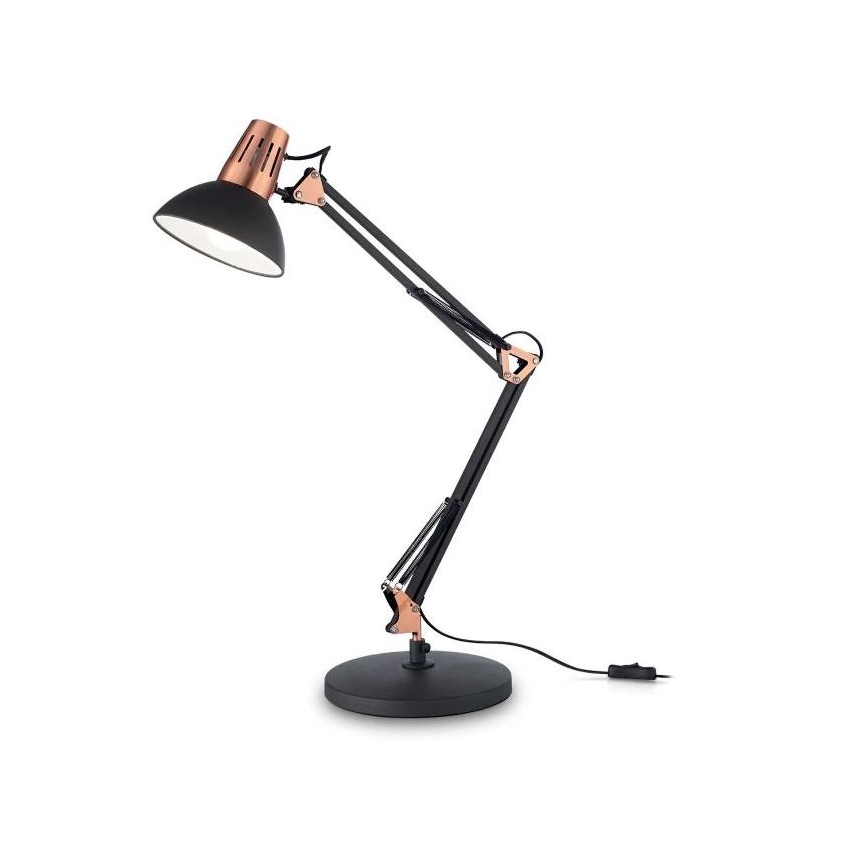 Stolová lampa s čiernym tienidlom a medenými prvkami stojí na čiernej podstave. Lampa je na dlhom, pohyblivom ramene. Elektrický kábel je pripojený k spodnej časti.
