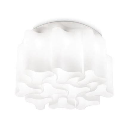 Biela stropná lampa s organickým tvarom visí v interiéri. Lampa osvetľuje priestor s dreveným stropom a hnedými dverami. V pozadí sú viditeľné schody s kovovými zábradlím.
