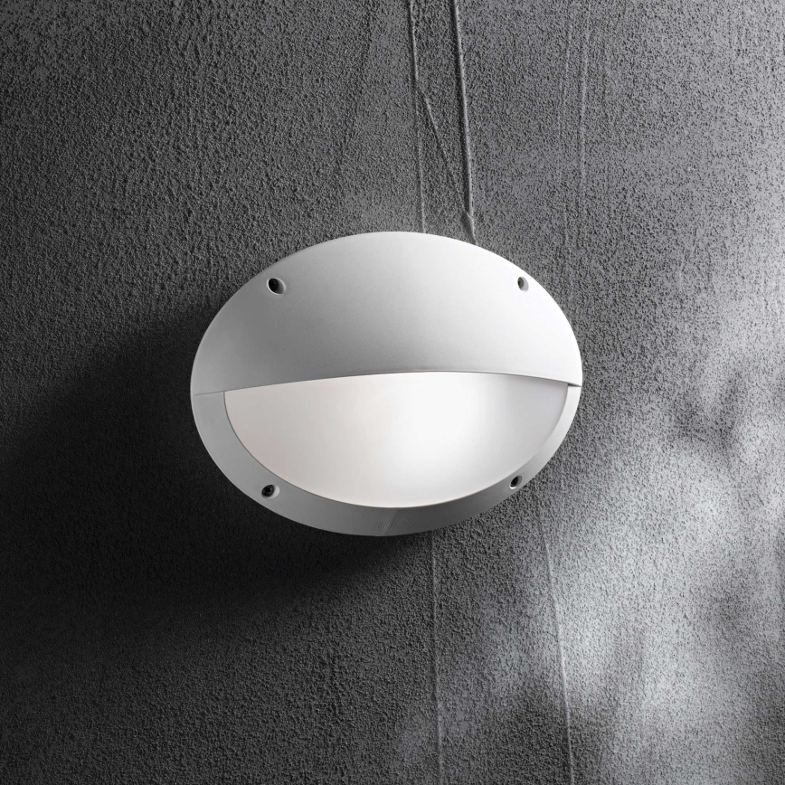 Biela oválna nástenná lampa je pripevnená na tmavosivej stene. Lampa je osvetľovacím telesom. Svetlo vyžaruje z jej vnútornej, mliečne bielej časti.