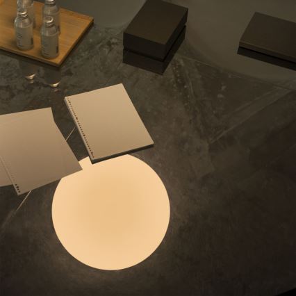 Dva bloky papiera ležia na tmavom stole. Na stole sú tiež tri fľaštičky a dve tmavé škatule. Pod papiermi svieti okrúhle svetlo.