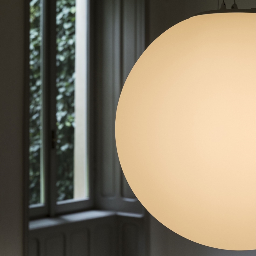 Guľová lampa visí v miestnosti. Svieti jemne. Na pozadí je rozostrené okno s výhľadom do zelene.