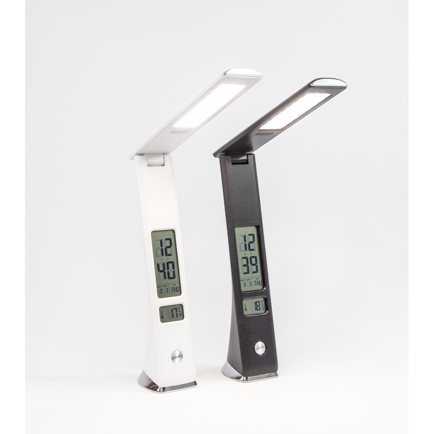 Dve stolové lampy s LED osvetlením a digitálnym displejom zobrazujúcim čas a teplotu stoja na bielom povrchu. Lampa vľavo je biela, vpravo čierna. Obe lampy sú sklopené.