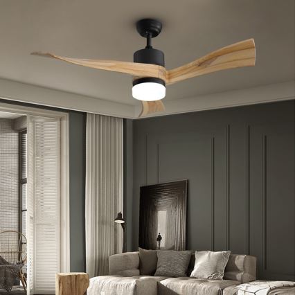 Drevený stropný ventilátor s čiernym krytom a LED osvetlením sa otáča. Je umiestnený v obývacej izbe s pohovkou, závesmi a tmavosivou stenou.