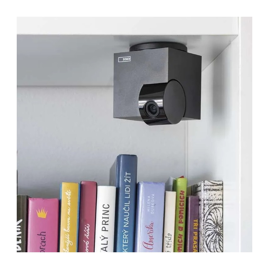 Bezdrôtová kamera Emos je pripevnená pod poličkou s knihami. Kamera sníma priestor pod poličkou. Knihy na poličke majú rôzne názvy a farby.