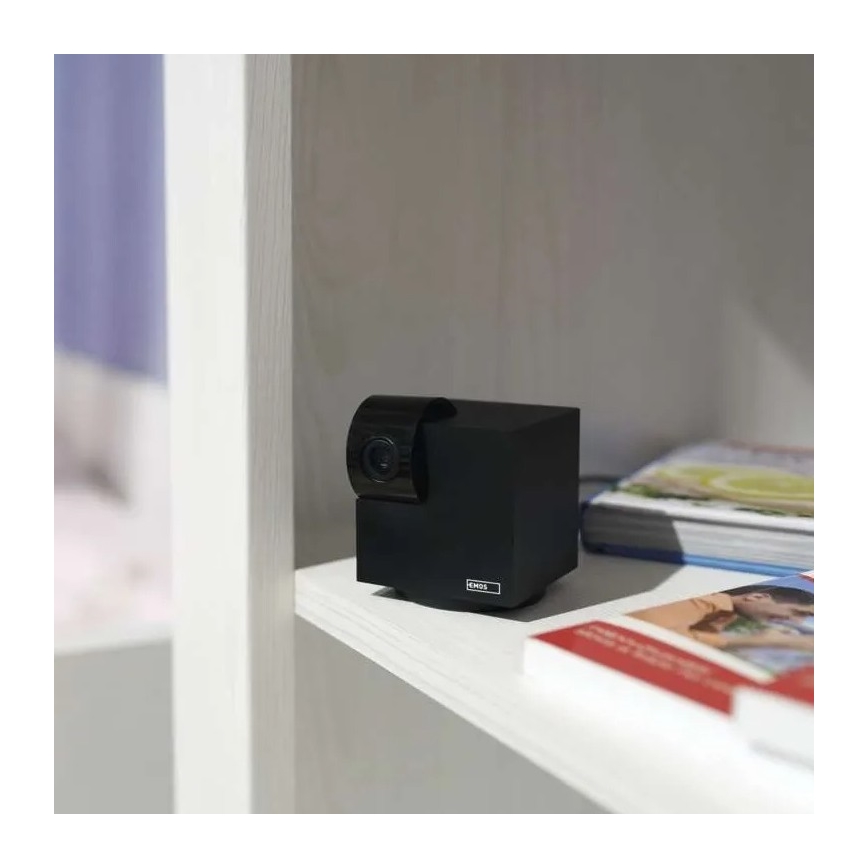 Čierna bezpečnostná kamera ENOS stojí na bielej poličke. Kamera je umiestnená vedľa kníh. Polička je súčasťou bielej knižnice.