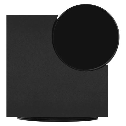 Čierny štvorcový podstavec s pripojeným čiernym okrúhlym prvkom stojí na malej čiernej podložke. Podstavec a okrúhly prvok sú spojené v pravom hornom rohu podstavca.