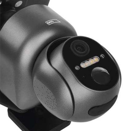 Šedá bezpečnostná kamera s objektívom a LED diódami sníma obraz. Na vrchnej časti je nápis „EMOS“. Kamera je umiestnená na neviditeľnej montážnej konštrukcii.