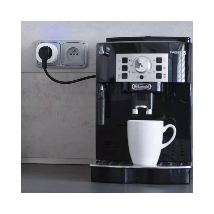 Espresso automat Delonghi Magnifica S je zapojený do inteligentnej zásuvky. Kávovar pripravuje kávu do bieleho hrnčeka. Celá scéna sa odohráva na kuchynskej linke.