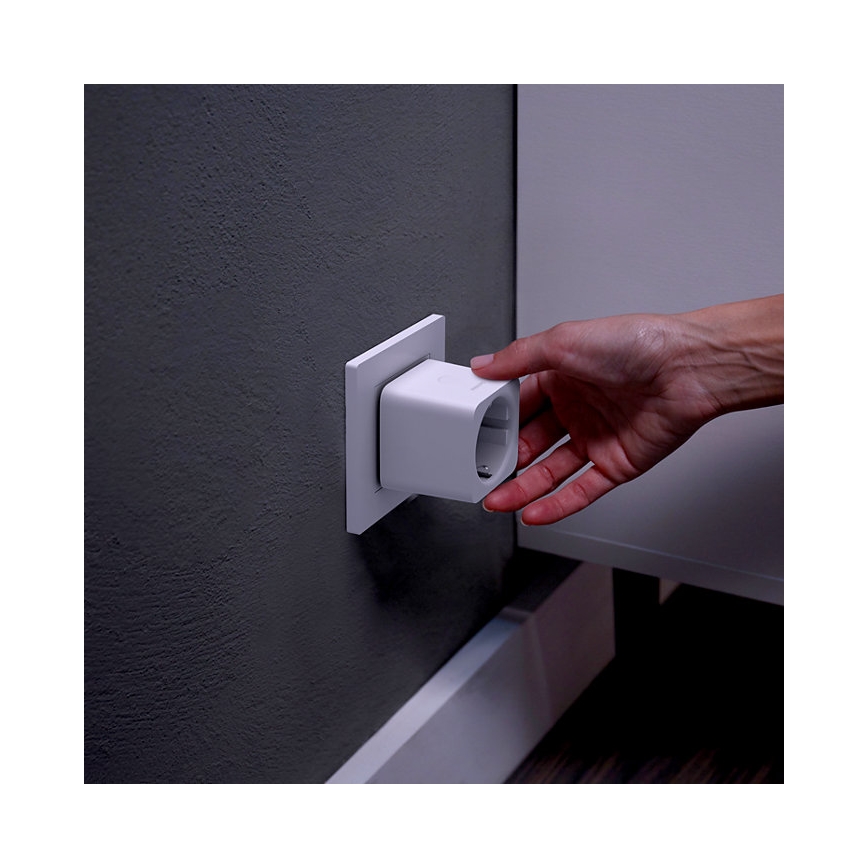 Ruka vkladá biely štvorcový adaptér do elektrickej zásuvky umiestnenej na tmavosivej stene. Adaptér je čiastočne zasunutý. Zásuvka je súčasťou bielej elektroinštalácie.
