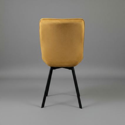 Žltá čalúnená stolička s prešívaným operadlom a sedadlom stojí na čiernych nohách. Stolička je zachytená z bočného pohľadu na bielom pozadí.