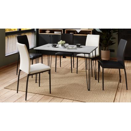 Obdĺžnikový jedálenský stôl s betónovou doskou a čiernymi kovovými nohami stojí na béžovom koberci. Okolo neho sú umiestnené štyri stoličky – dve čierne a dve svetlo béžové. Prostredie tvorí svetlá drevená podlaha a časť jedálne.