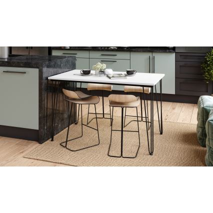 Biely jedálenský stôl s kovovými nohami a drevenými barovými stoličkami stojí na svetlohnedej rohoži v kuchyni s bledomodrou a tmavou kuchynskou linkou. Na stole sú šálky, váza a kniha.