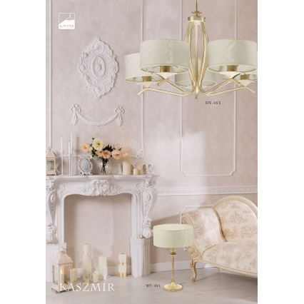 Zlatá luster s piatimi krémovými tienidlami visí v miestnosti s bielym krbom a krémovou pohovkou. Na stolčeku stojí stolová lampa s krémovým tienidlom. Kódy produktov: 1275 + KS 5 a 1277 + KS L.