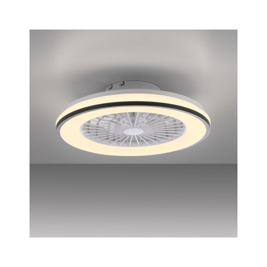 Biely stropný ventilátor s LED osvetlením je pripevnený k stropu. Ventilátor má okrúhly tvar s bielymi lopatkami a vonkajším svetelným kruhom. Je umiestnený v jednoducho zariadenej miestnosti.