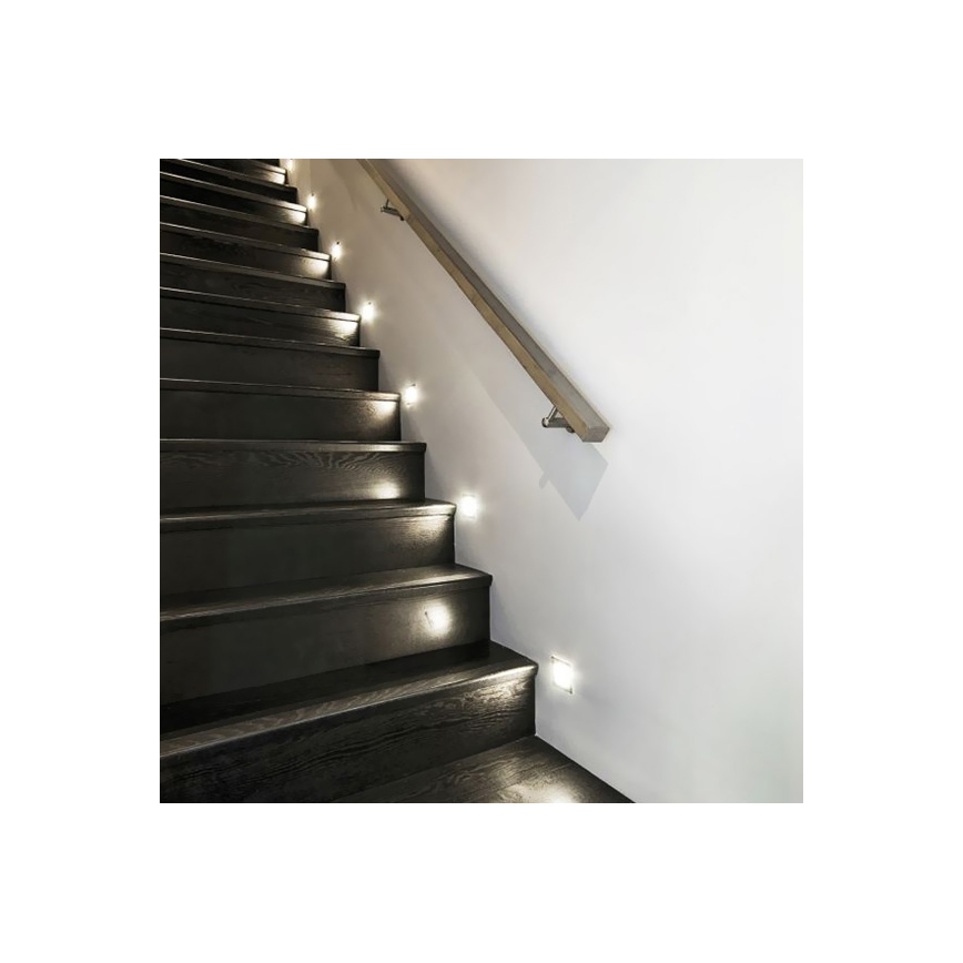 Tmavé drevené schodisko osvetľujú malé vstavané svetlá. Svetlá sú umiestnené pozdĺž steny s dreveným zábradlím.