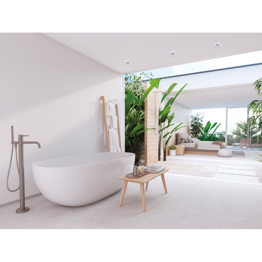 Vanička stojí v minimalistickej kúpeľni. Pri nej je drevený stolík s uterákmi. Za vaňou je otvorený priestor s tropickou záhradou a spálňou.