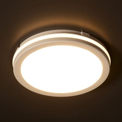 Okrúhle stropné svetlo svieti. Biele telo má dvojitý okraj. Svetlo je inštalované na tmavom strope.