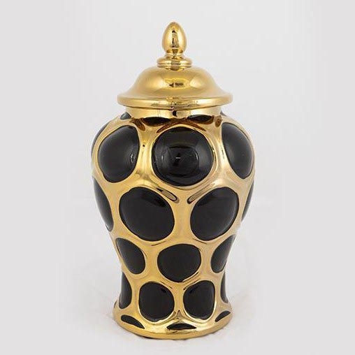 Keramická váza s viečkom stojí na svetlom podklade. Váza je čierna s okrúhlymi zlatými detailmi. Viečko je zlaté.