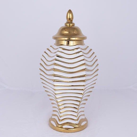 Keramická váza s viečkom stojí na bielom podklade. Váza je prevažne biela s vertikálnymi zlatými pruhmi v tvare vĺn. Viečko je zlaté.