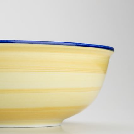 Žltá misa s modrým lemom stojí na svetlom povrchu. Misa má pruhovaný vzor.
