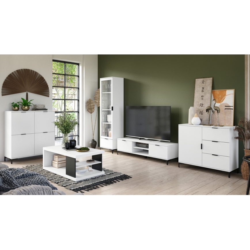 Biely nábytok je umiestnený v obývacej izbe. Súčasťou je televízna zostava, konferenčný stolík, vysoká vitrína a komoda. Nábytok je moderný, s tmavými kovovými nožičkami. Izba má svetlú podlahu a olivovozelenú stenu.