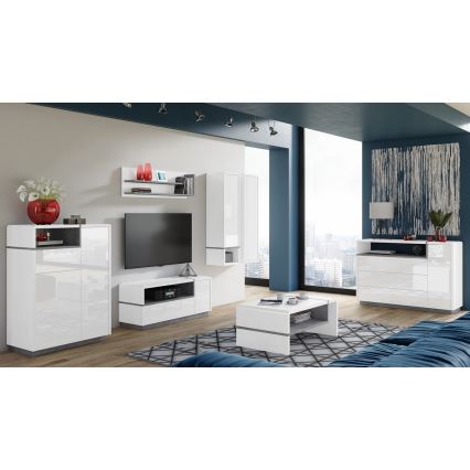 Biela moderná zostava nábytku do obývačky obsahuje televízny stolík, vysokú skrinku, nízkú skrinku, konferenčný stolík a poličku. Nábytok je umiestnený v priestore s veľkým oknom a tmavomodrou stenou.