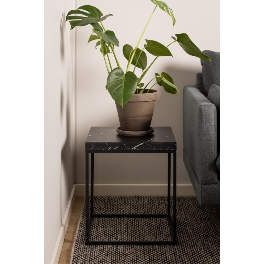 Čierny odkladací stolík s mramorovou doskou stojí na tmavej koberec v rohu miestnosti pri sedačke. Na stolíku je umiestnená izbová rastlina v hlinenom kvetináči.