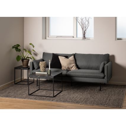 Dva čierne odkladacie stolíky s mramorovou doskou stoja pred sivou sedačkou na tmavom koberci v obývacej izbe. Na väčšom stolíku je sviečka a dekoračné predmety.