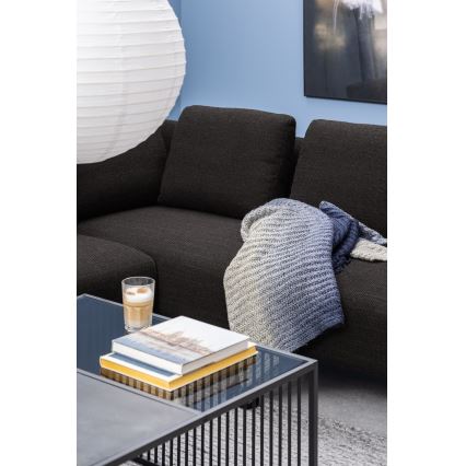 Rohová tmavosivá sedačka s prehodenou svetlomodrou dekou leží v miestnosti s modrou stenou a bielym papierovým lampášom. Na nízkom sklenenom kávovom stolíku je pohár cappuccina a niekoľko kníh.