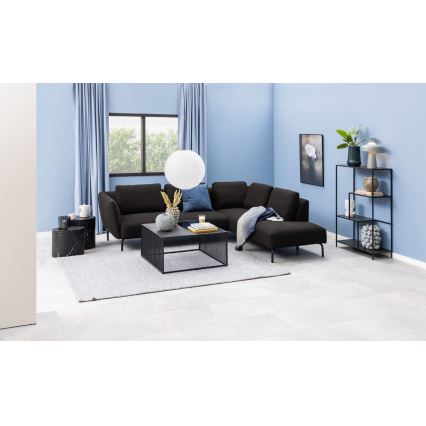 Rohová sedačka stojí v obývacej izbe s bledomodrými stenami. Na koberci pred ňou je konferenčný stolík. V miestnosti je aj regál a dve malé stolíky.