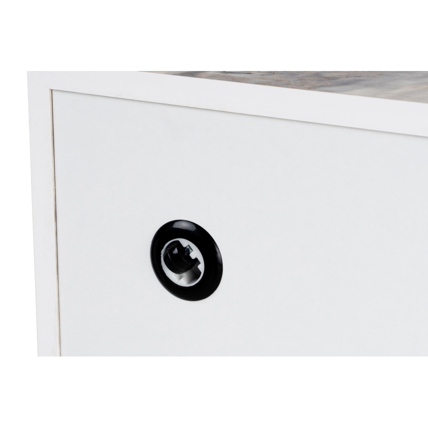 Biela skrinka s čiernym vývodom je zobrazená zblízka. Vrch skrinky je z iného materiálu, svetlejšieho dreva. Čierny vývod je umiestnený na prednej strane bielej plochy.