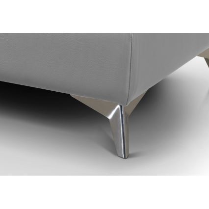 Šedá pohovka stojí na strieborných kovových nožičkách v tvare klinu. Nožičky sú umiestnené na svetlej podlahe.