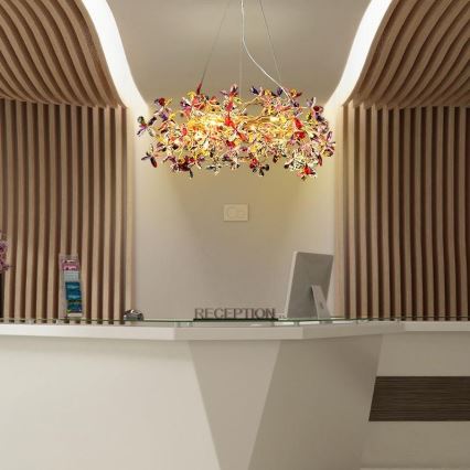 Lampa s tvarom kvetov visí nad recepciou. Recepcia je biela s nápisom „RECEPTION“. Po stranách recepcie sú drevené steny.