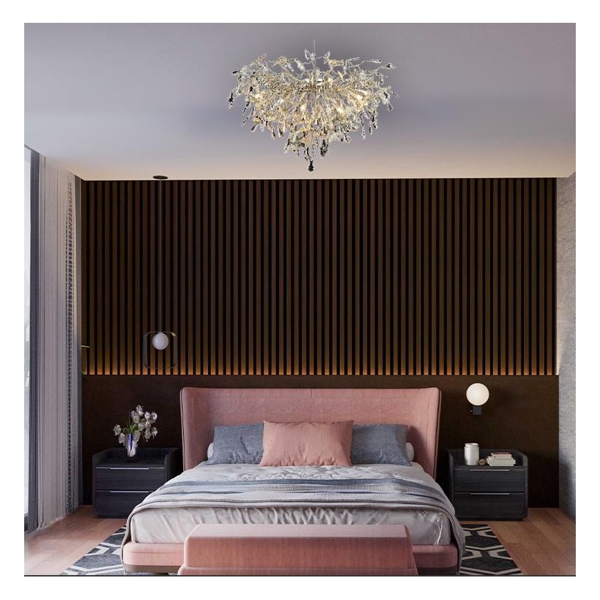 Luster svieti v spálni. Je inštalovaný na strope nad ružovou posteľou s posteľnou bielizňou a vankúšmi. Stena za posteľou je tmavohnedá s vertikálnymi lamelami.