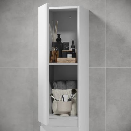 Biela kúpeľňová skrinka s otvorenými dvierkami odhaľuje police s kozmetikou, uterákmi a doplnkami. Na policiach sú fľaše, sviečky, aromatické tyčinky a kozmetické štetce v nádobke. Skrinka je umiestnená v kúpeľni s šedými obkladačkami.