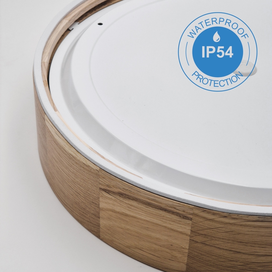 Svietidlo s dreveným rámom a bielym difúzorom. Je čiastočne viditeľná zadná strana. Na difúzore je označenie „WATERPROOF IP54 PROTECTION“.