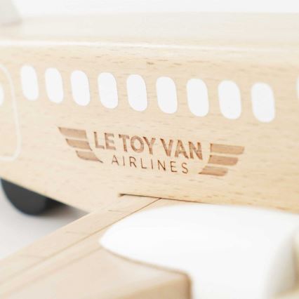 Drevené lietadlo s vygravírovaným logom „LE TOY VAN AIRLINES“ a bielymi okienkami na trupe. Lietadlo je statické, položené na bielom povrchu.