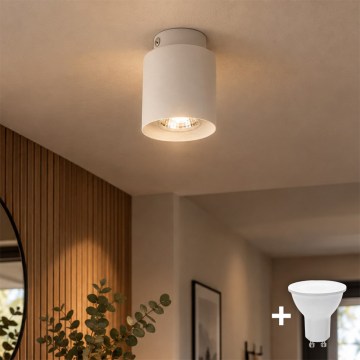 Biela stropná lampa svieti. Je valcovitého tvaru s integrovaným svetlom. Upevnenie je na vrchu.