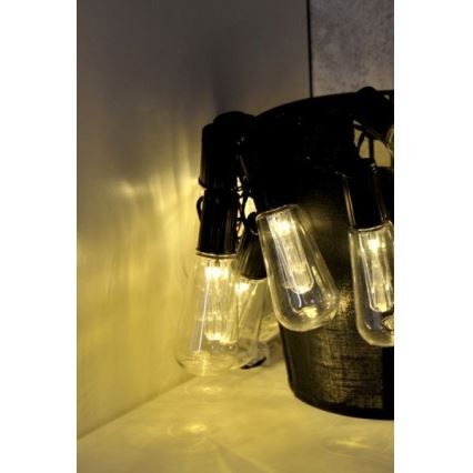 Svietiace LED žiarovky s tvarom Edisonových žiaroviek na čiernom kábli svietia v teplej bielej farbe. Žiarovky sú zavesené v čiernom koši.