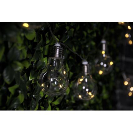 Sklenené žiarovky svietia na svetelnom reťazi. Žiarovky sú zavesené na tmavozelenej umelej stene. Svetlo vyžaruje teplú žltú farbu.