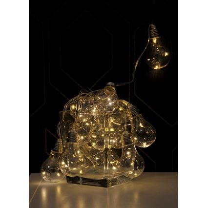 Svetelný reťaz s LED žiarovkami v tvare klasických žiaroviek je umiestnený v sklenenej váze. Žiarovky svietia teplým svetlom. V pozadí je tmavá stena s geometrickým vzorom.