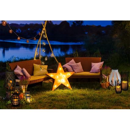 Hviezda svietiaca LED diódami stojí pred dvoma záhradnými sedačkami na trávnatej ploche pri jazere. Okolie je osvetlené lampášmi a girlandami.