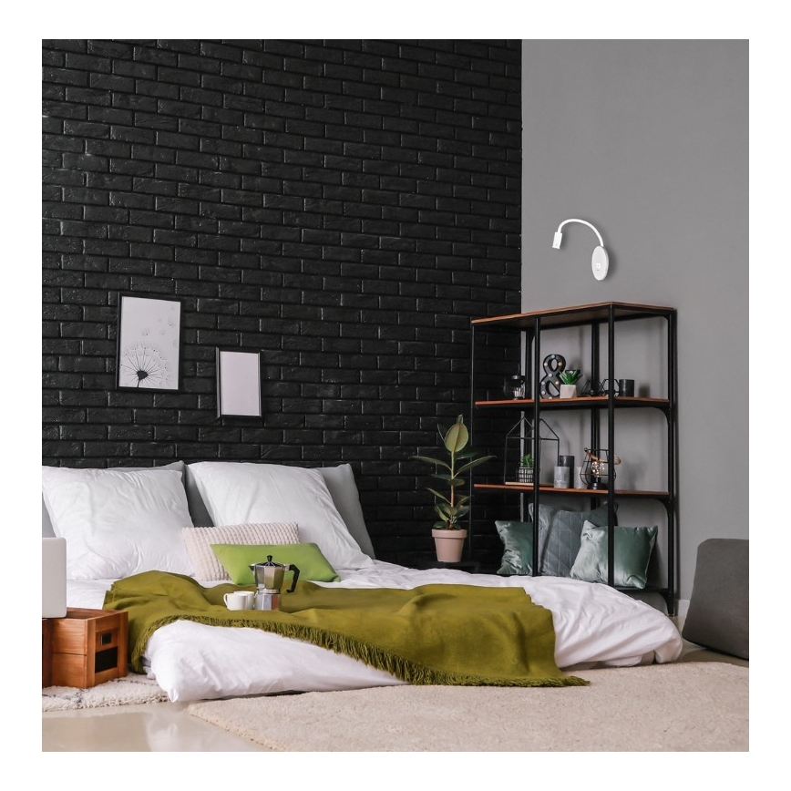 Malá nástenná lampa s ohybným ramenom je pripojená k zásuvke s dvoma otvormi a USB portom. Lampa svieti na šedú plochu.