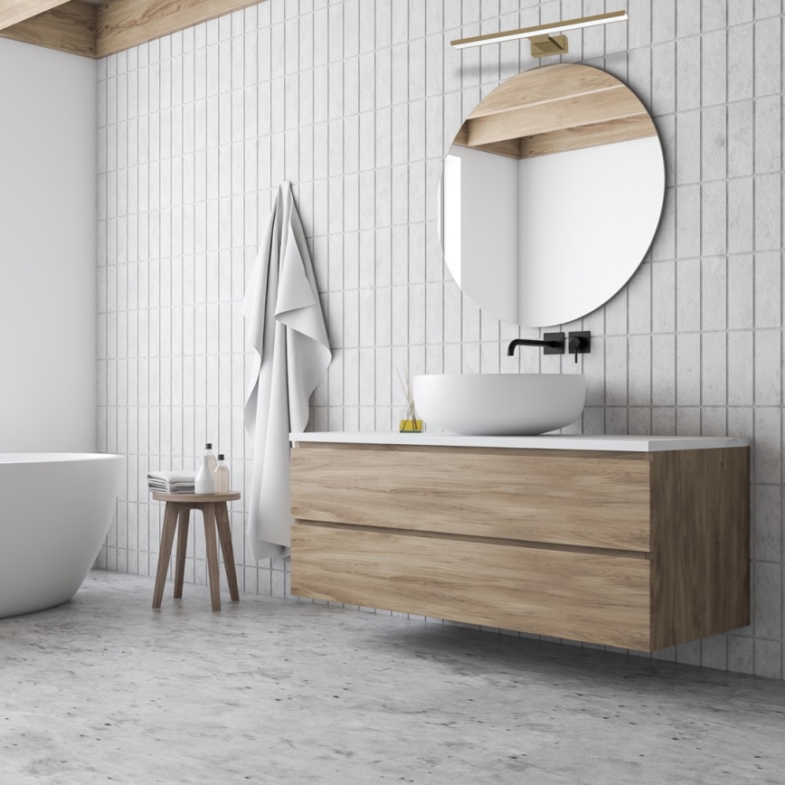 Svetlo svieti nad umývadlom v tmavošedej kúpeľni. V kúpeľni je aj voľne stojaca vaňa a nábytok so zásuvkami.