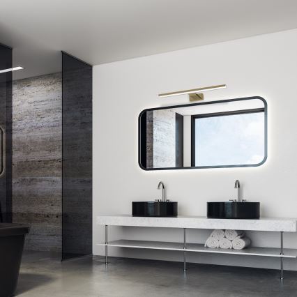 Drez s batériou je umiestnený na drevenom nábytku v kúpeľni. Zrkadlo s osvetlením visí nad drezom. Steny sú obložené svetlým drevom.