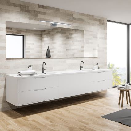 Dvojité umývadlo s bielou skrinkou je umiestnené v kúpeľni. Nad umývadlom je zavesené zrkadlo s osvetlením. Kúpeľňa má svetlé obklady a drevenú podlahu.