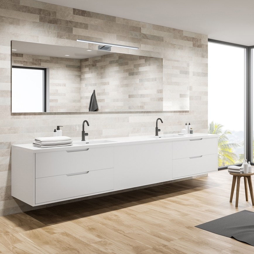 Dvojité umývadlo s bielou skrinkou je umiestnené v kúpeľni. Nad umývadlom je zavesené zrkadlo s osvetlením. Kúpeľňa má svetlé obklady a drevenú podlahu.